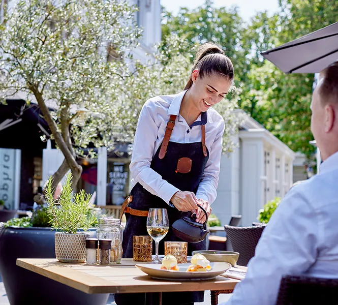 Waitress serving food and drinks on the sunny terrace of Restaurant Sophia at the Carlton Ambassador Hotel in The Hague.