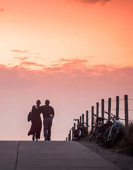 Koppel wandelend in de duinen bij zonsondergang